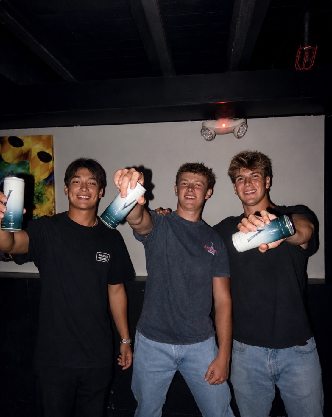 Three friends holding out VYRE cans on a night out