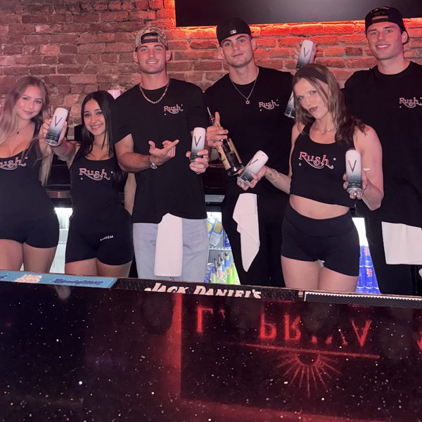 Rush bar staff holding VYRE cans behind the bar